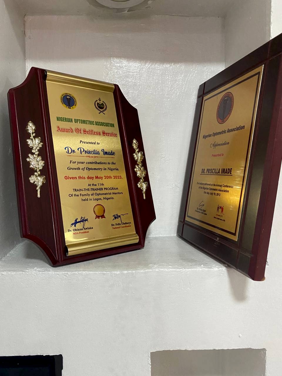 Two framed award plaques presented to Dr. Priscilia Imade, mounted on the clinic wall.