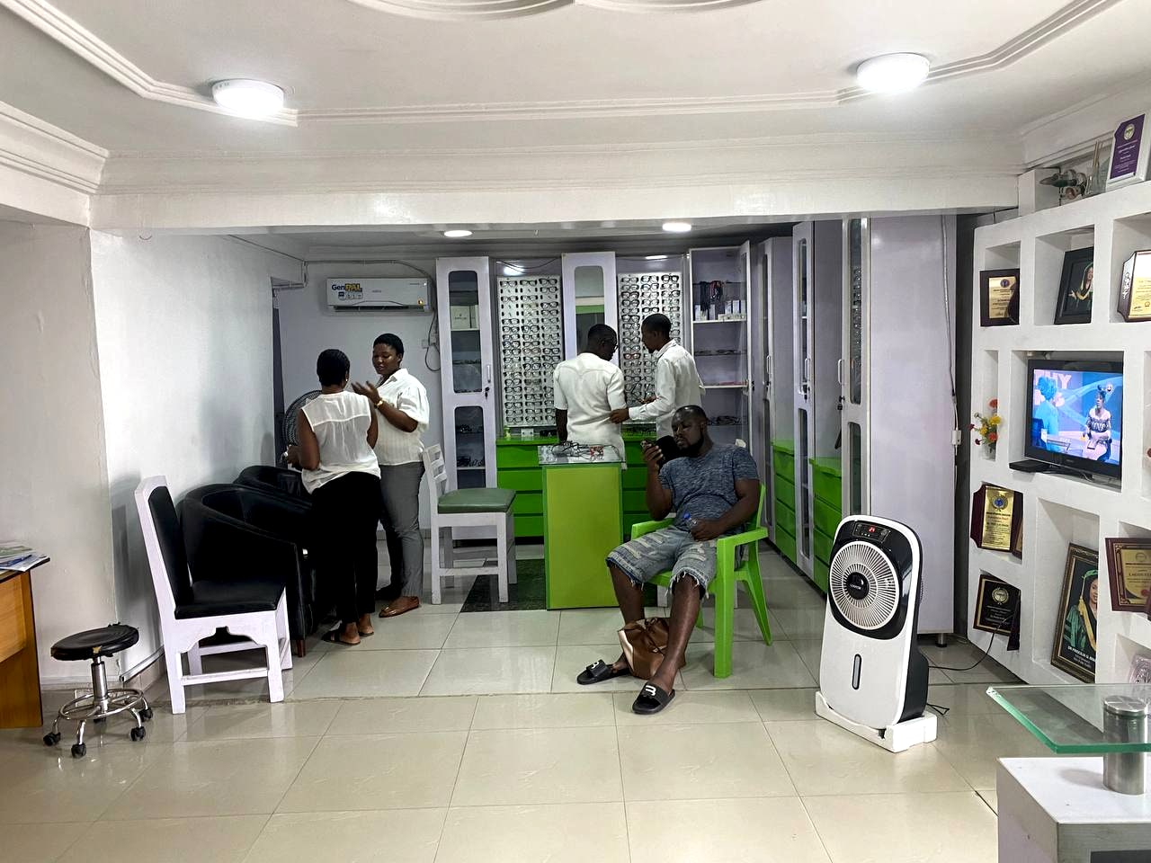 The clinic's front room, with patients seated along one wall, staff at the display cabinets, and framed certificates covering the far wall.