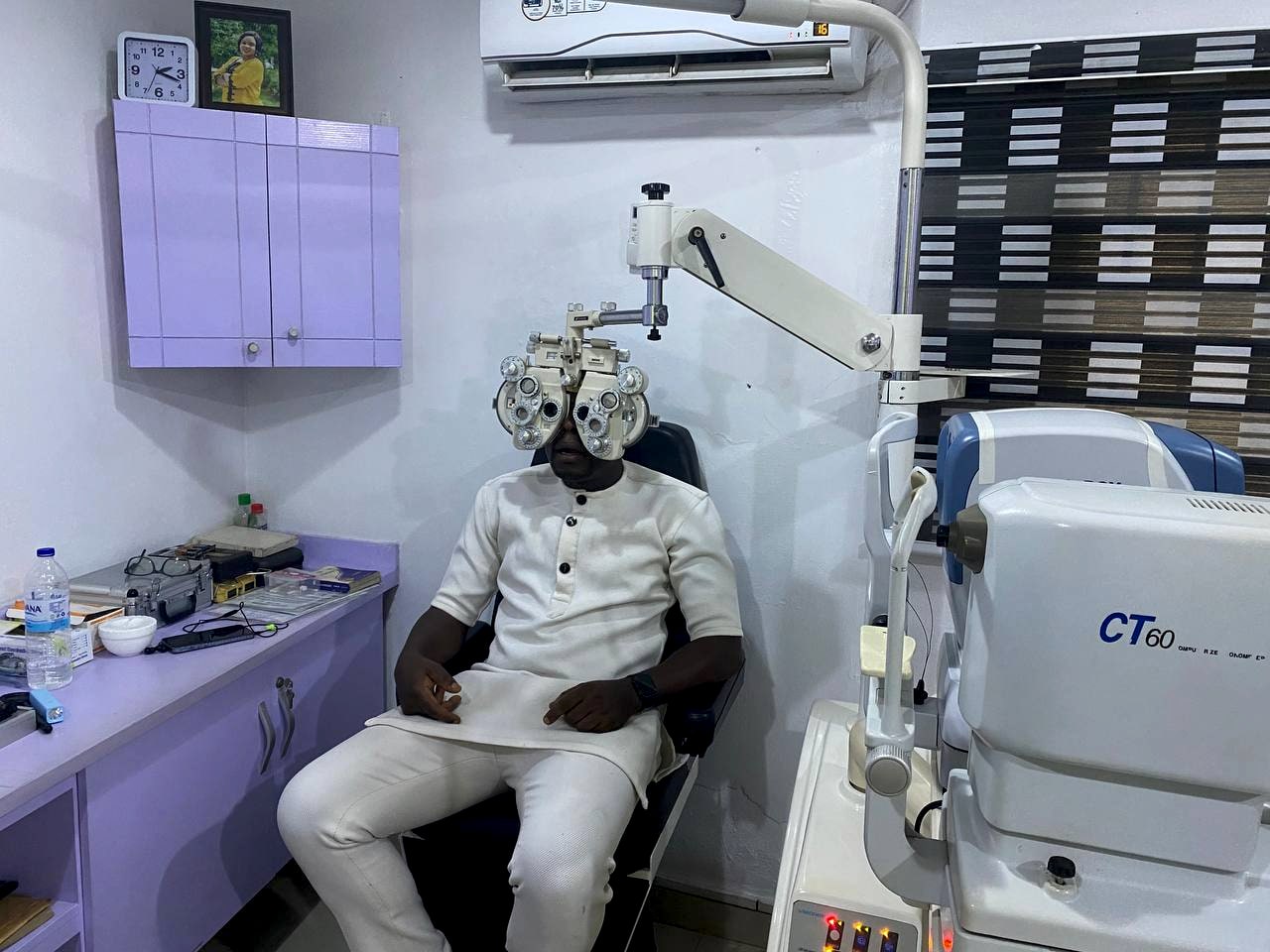 A patient seated in the examination chair with a phoropter swung beside him and a non-contact tonometer on the bench.