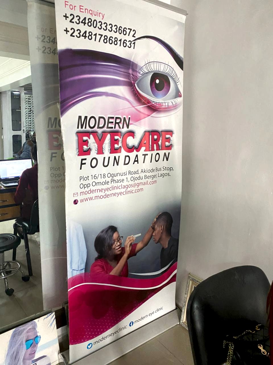 A Modern Eyecare Foundation roll-up banner standing in the clinic, carrying the Foundation's name and the clinic's two telephone numbers.